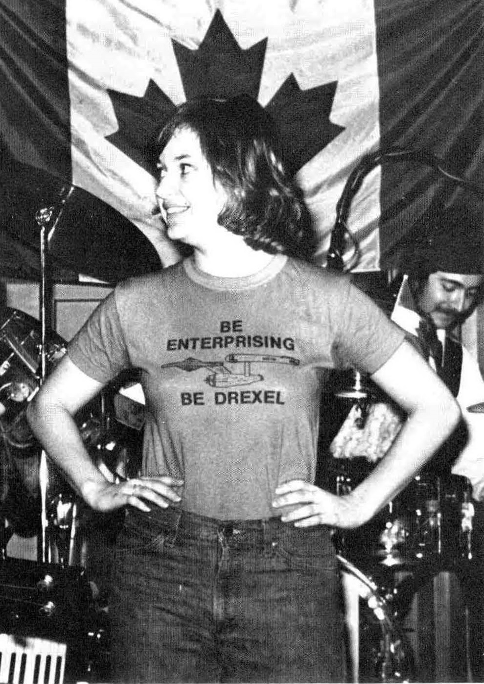 A woman stands in front of the Canadian flag and a drum kit